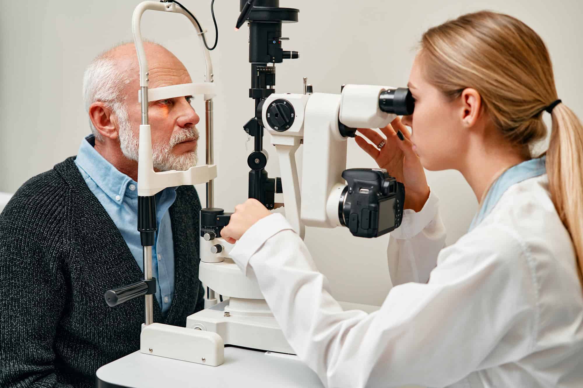 blonde Augenärzting untersucht die Augen eines älteren Mannes mit weißem Haar
